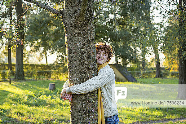 Smiling young man hugging tree at park
