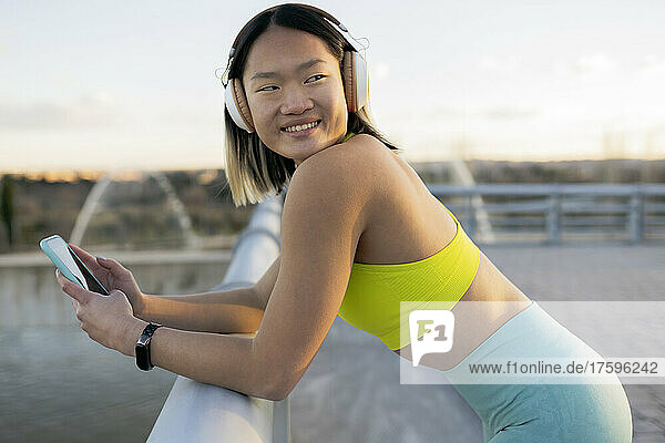 Smiling woman with smart phone listening music on headphones