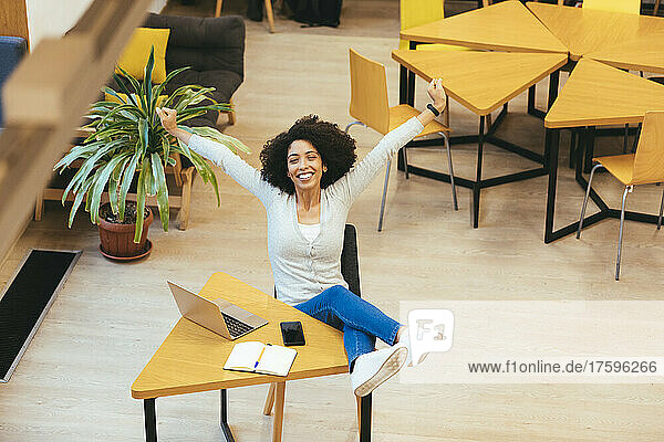Businesswoman with arms outstretched sitting in creative office