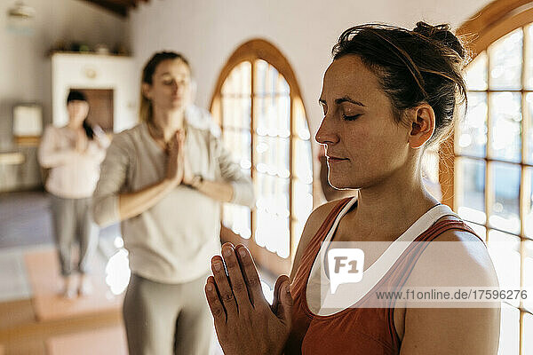 Yoga instructor meditating with hands clasped in class