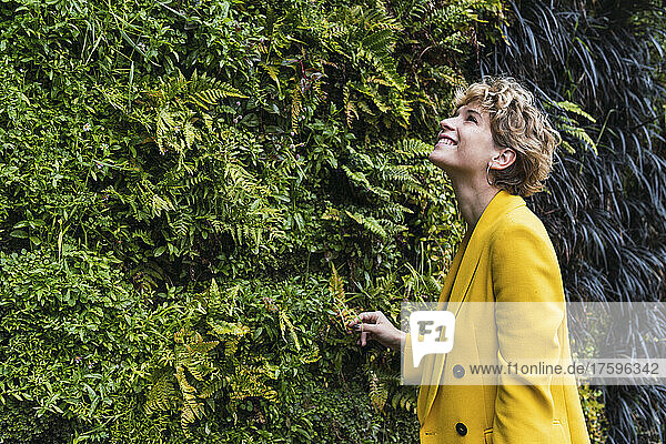Smiling woman standing by green plants in public park