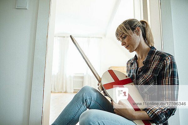 Woman sitting with wooden sword and shield at home