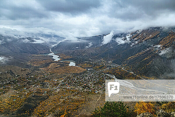 Russia  Dagestan  Gunib  Low clouds over Caucasus Mountains in autumn with village and reservoir in background