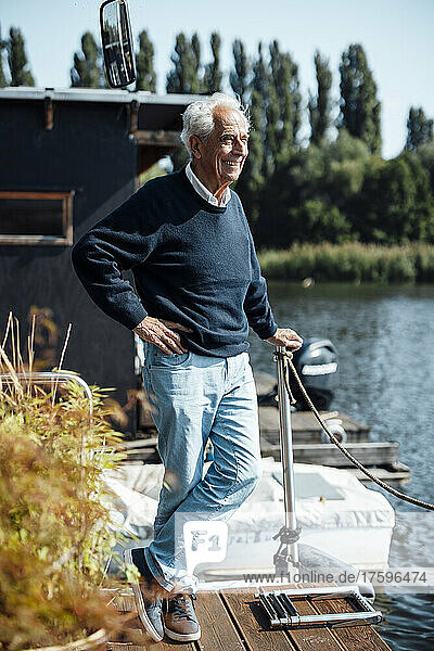 Happy senior man with hand on hip standing at houseboat