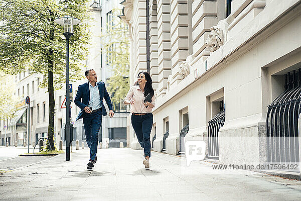 Businessman and businesswoman running on footpath in city