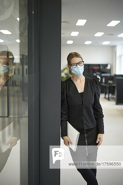 Businesswoman with laptop wearing protective face mask in office