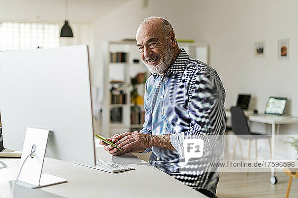 Cheerful businessman with mobile phone sitting at desk