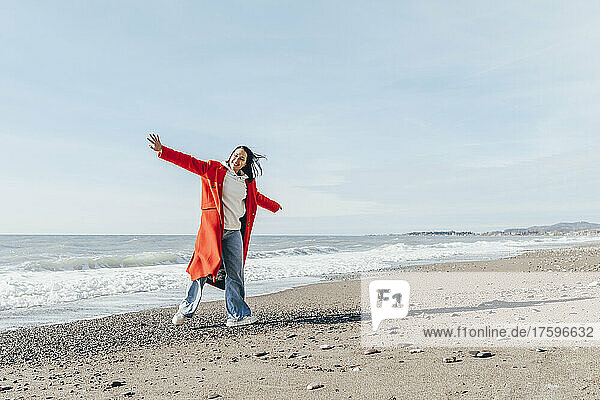 Cheerful woman with arms outstretched by dog at beach