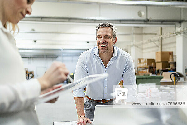 Happy businessman looking at businesswoman using tablet PC in industry