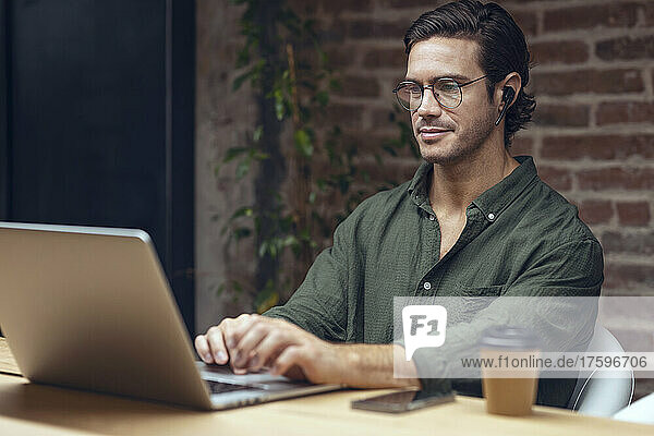 Confident creative businessman using laptop at desk in office