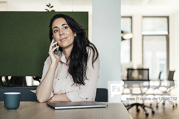 Businesswoman talking on smart phone at desk in coworking office