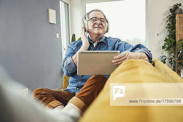 Senior man with eyes closed listening music through wireless headphones on sofa in living room