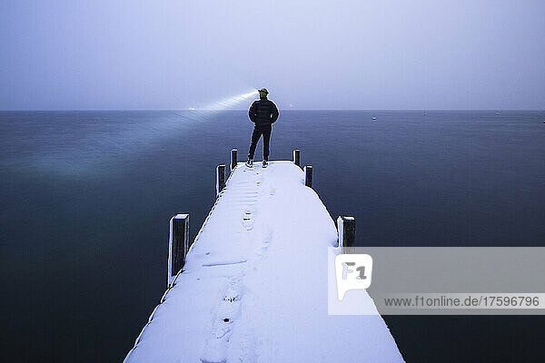 Tourist with headlamp admiring lake standing on jetty in winter  Walchensee  Bavaria  Germany