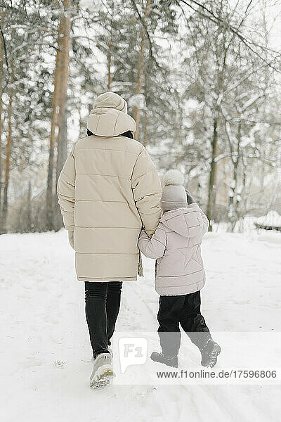 Mutter und Tochter gehen gemeinsam auf Schnee im Winterwald spazieren