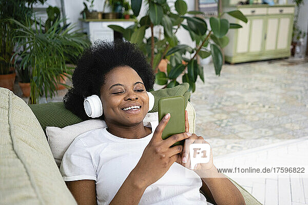 Happy woman using smart phone and listening music on sofa in living room