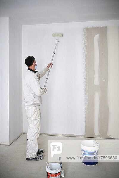 House painter painting wall with roller at construction site