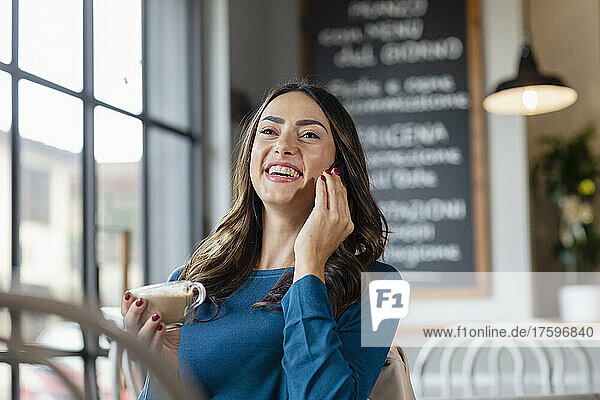 Junge Frau telefoniert mit Smartphone und trinkt Kaffee im Café
