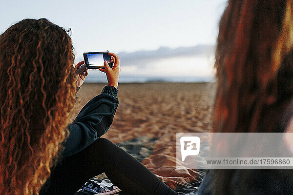 Junge Frau fotografiert mit Smartphone von Freund am Strand