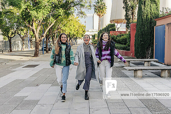 Cheerful friends holding hands and walking in city