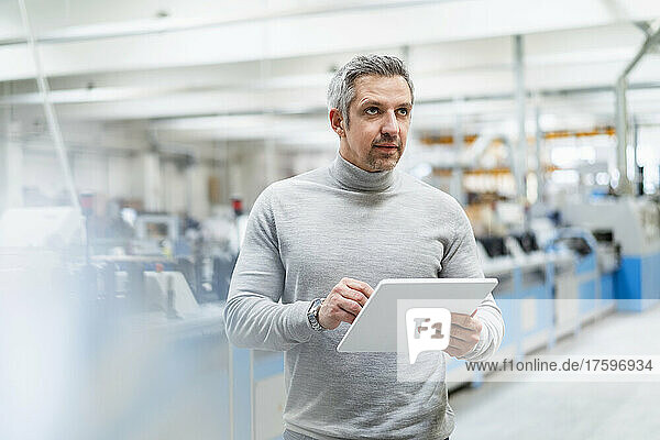 Thoughtful businessman with tablet PC in factory
