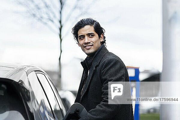 Smiling man with black hair standing by electric car