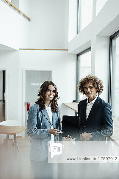 Smiling businessman and businesswoman with tablet PC standing in office