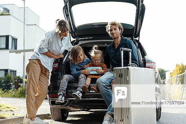 Mother looking at children sitting by father in car trunk