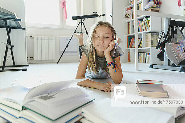 Girl looking at books lying on floor at home