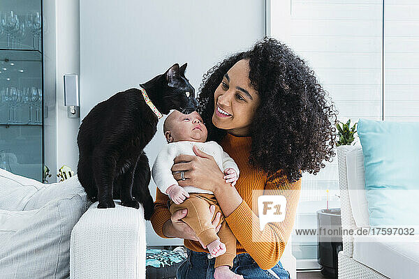 Smiling mother with baby boy looking at cat in living room