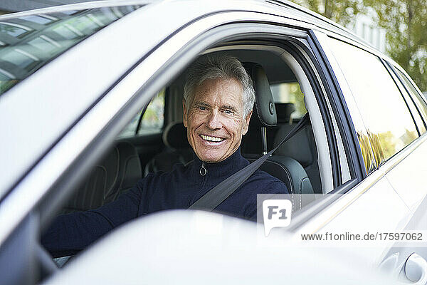 Smiling elderly man sitting in car on road trip