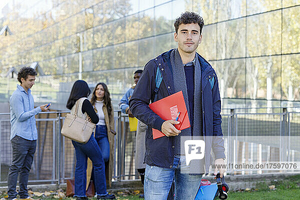 Young man holding file with students in background at campus