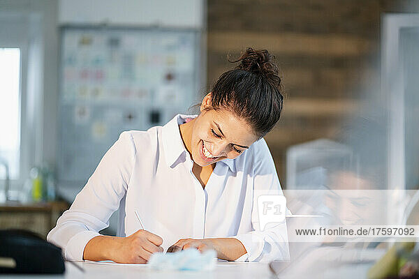 Smiling businesswoman writing in note pad at desk