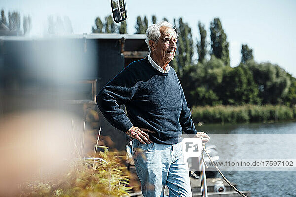 Smiling senior man standing with hand on hip at houseboat