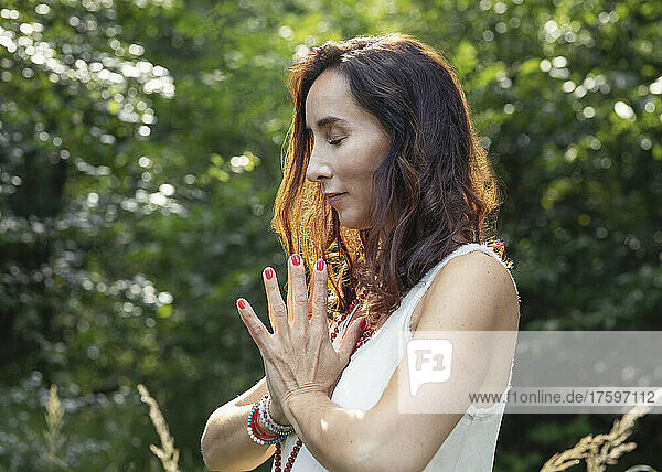 Woman with eyes closed and hands clasped meditating in nature