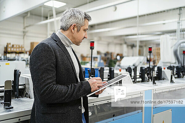 Businessman with tablet PC analyzing machinery in factory