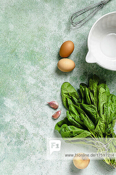 Studio shot of bowl  egg beater and various vegetables lying against green background