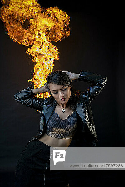 Woman standing with hands behind head against fire in studio