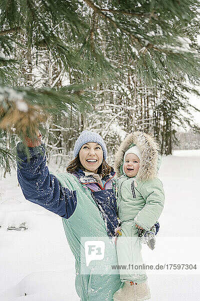 Smiling woman carrying daughter pointing at tree in winter
