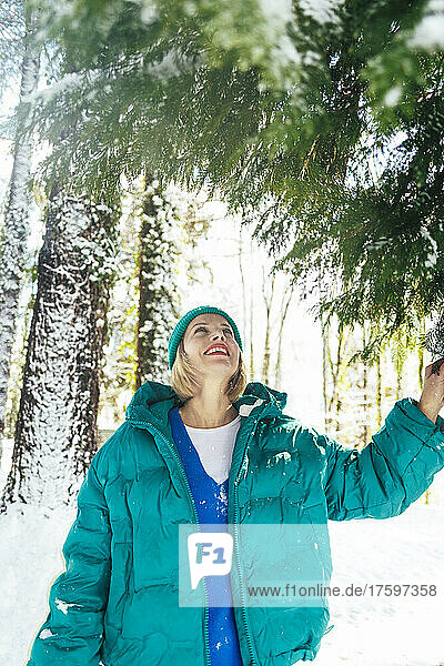 Smiling woman standing below fir tree in winter forest