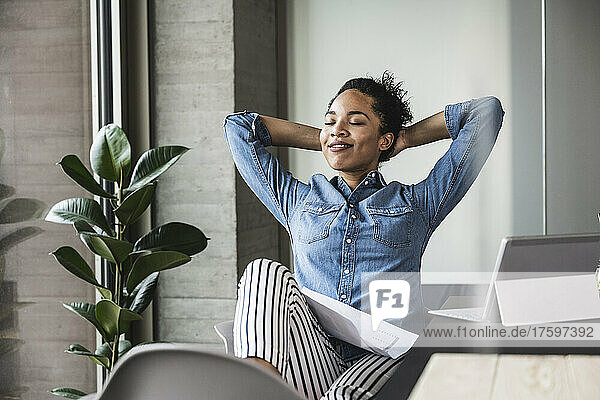 Young businesswoman relaxing with hands behind head in office