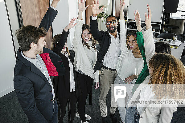 Happy business colleagues with arms raised in coworking office