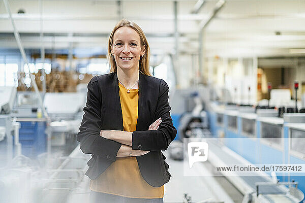 Happy businesswoman with arms crossed standing in factory