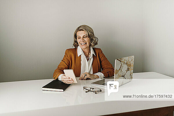 Happy businesswoman surfing net through smart phone at desk