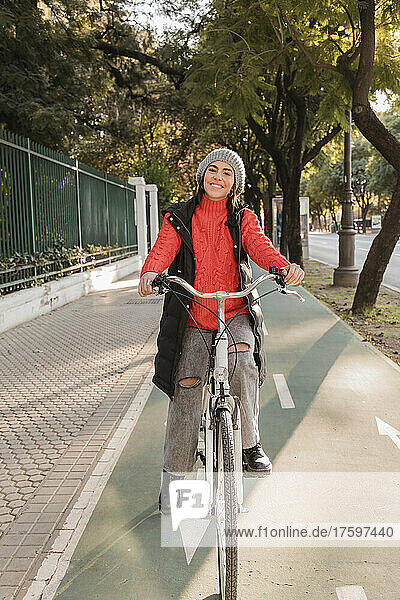 Smiling young woman cycling on bicycle lane