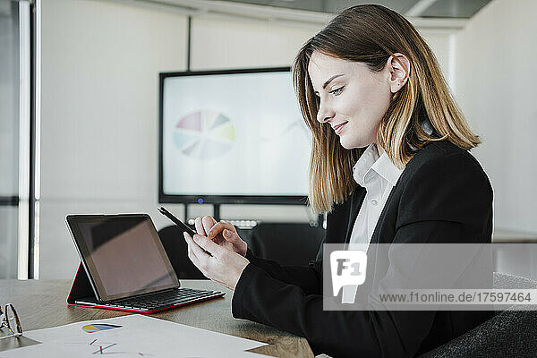 Smiling businesswoman using smart phone by tablet PC in office