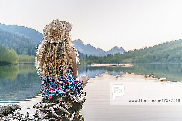 Woman with straw hat sitting by lake on vacation
