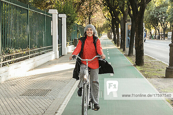 Smiling young woman cycling on bicycle lane