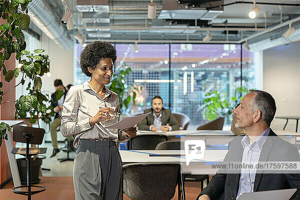 Businesswoman discussing with colleague over document at coworking space