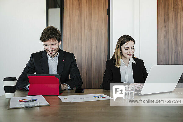 Smiling business colleagues using wireless technologies at desk in coworking office