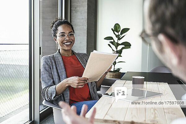 Smiling businesswoman holding documents discussing with colleague in office